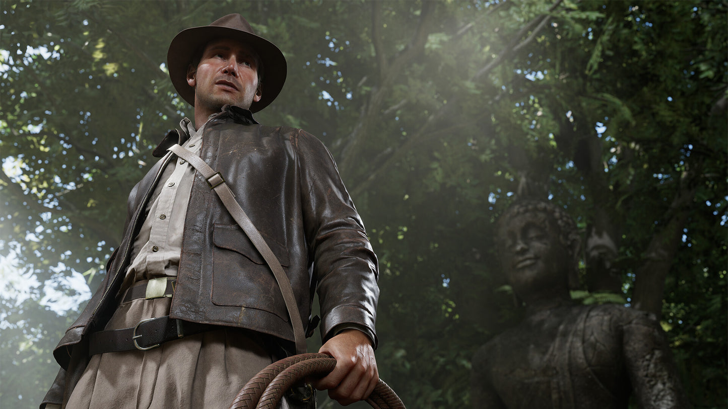 Man in a leather jacket and hat standing next to a statue in a forest setting