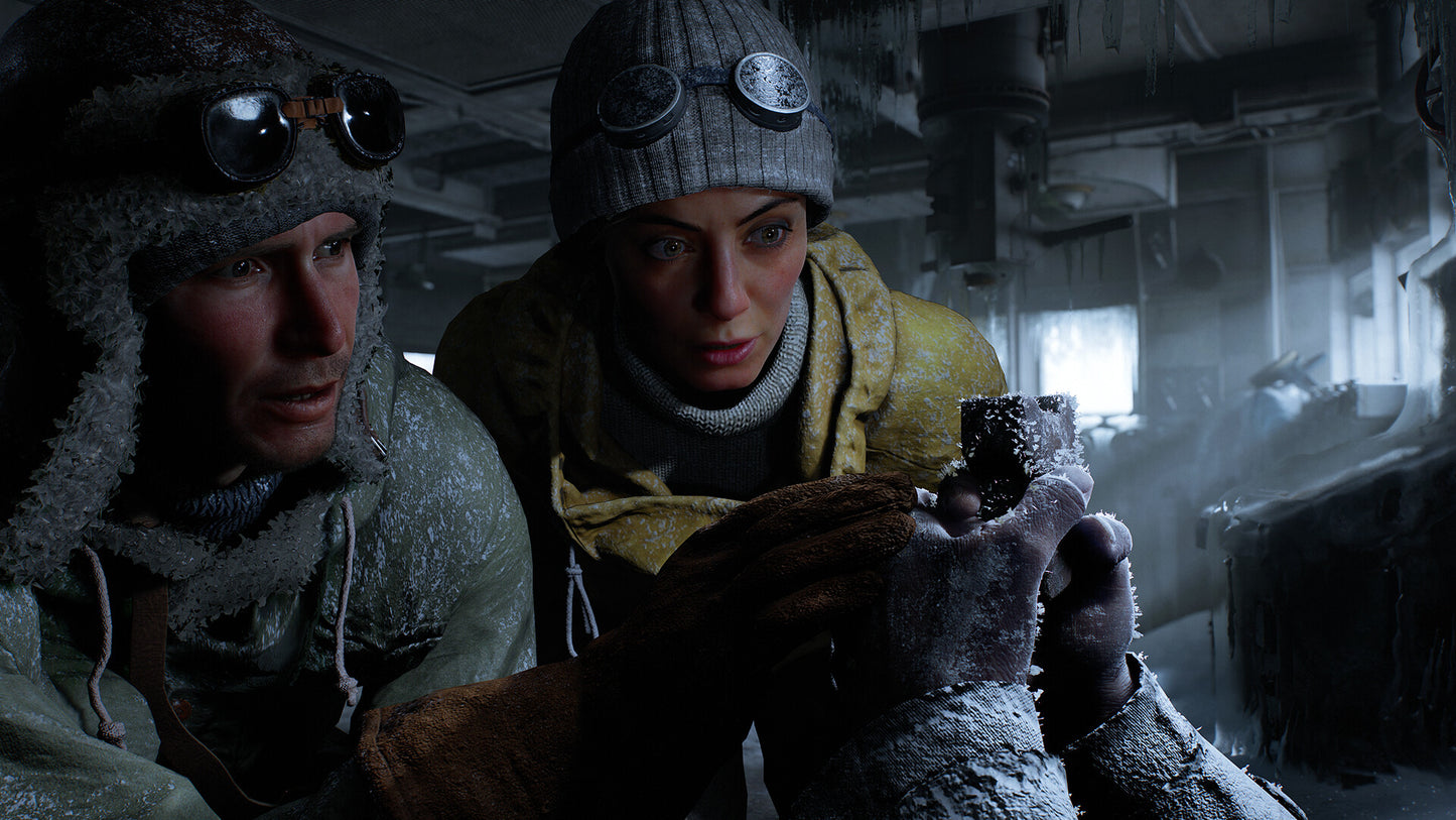 Two people in cold-weather gear looking at a device in a snowy interior setting