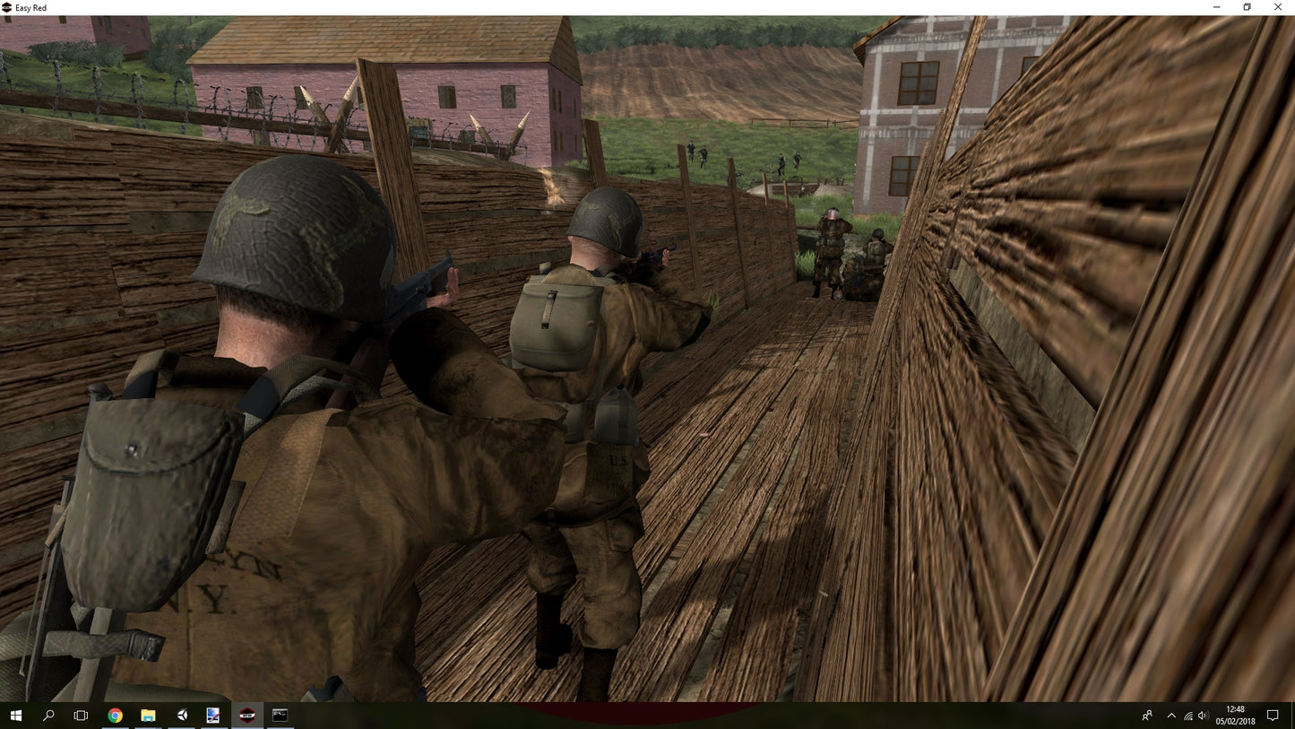 Two soldiers in a military setting with wooden structures and buildings in the background.