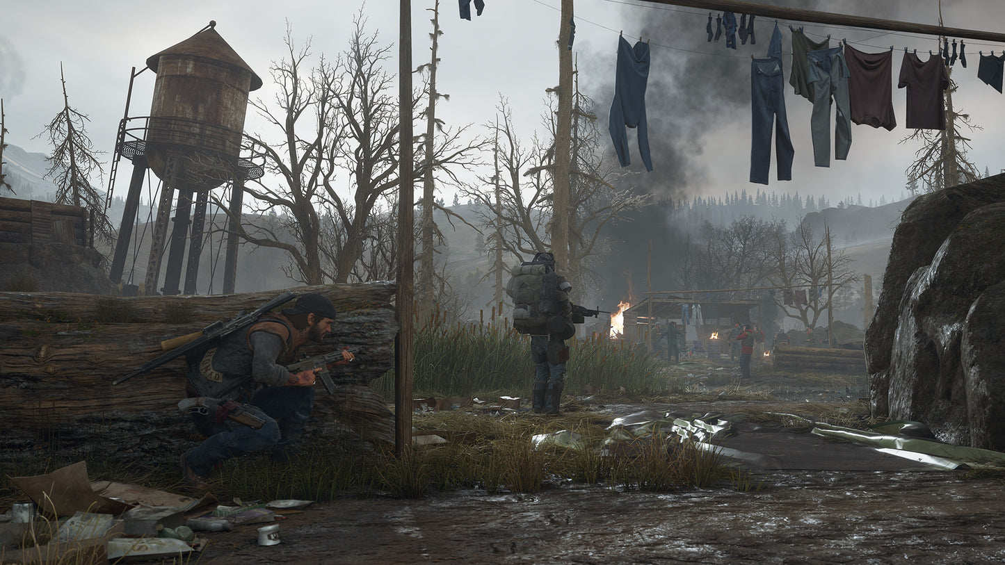 Two characters in a post-apocalyptic setting with a wooden structure, clothes hanging, and a fire in the background.