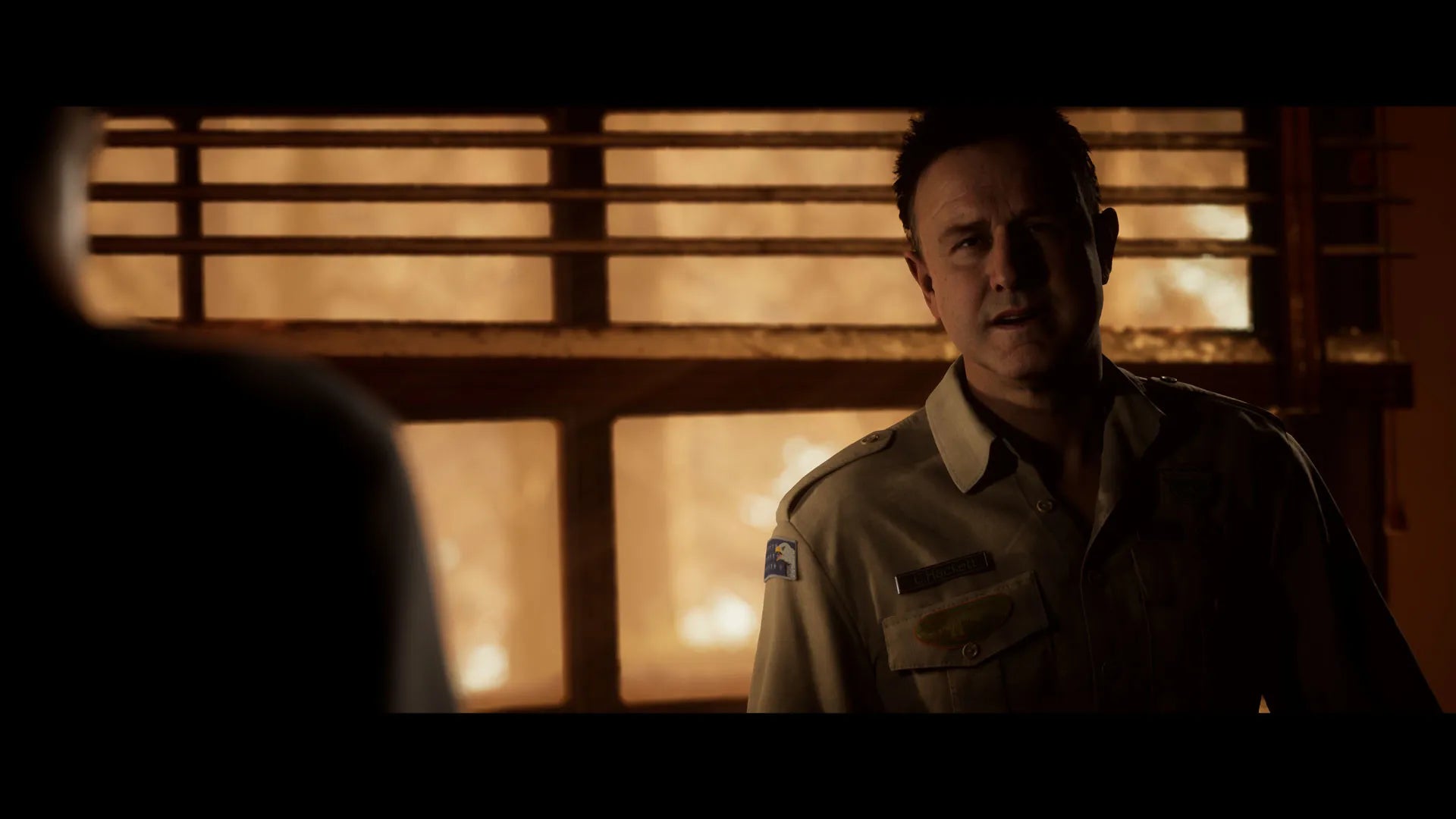Man in a uniform standing in a dimly lit room with wooden paneling.