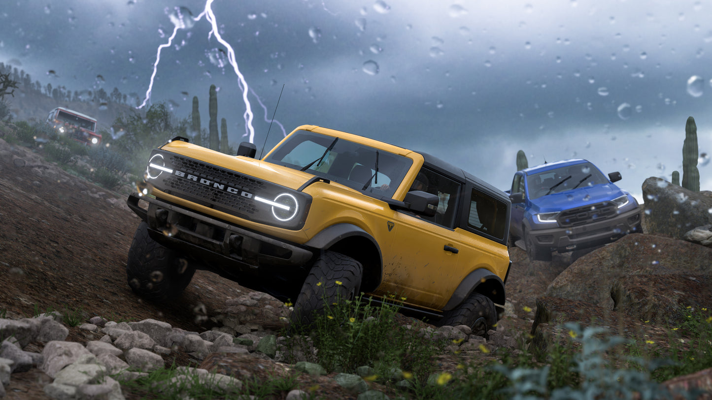 Yellow Ford Bronco off-road vehicle driving through a rocky landscape with another vehicle in the background.