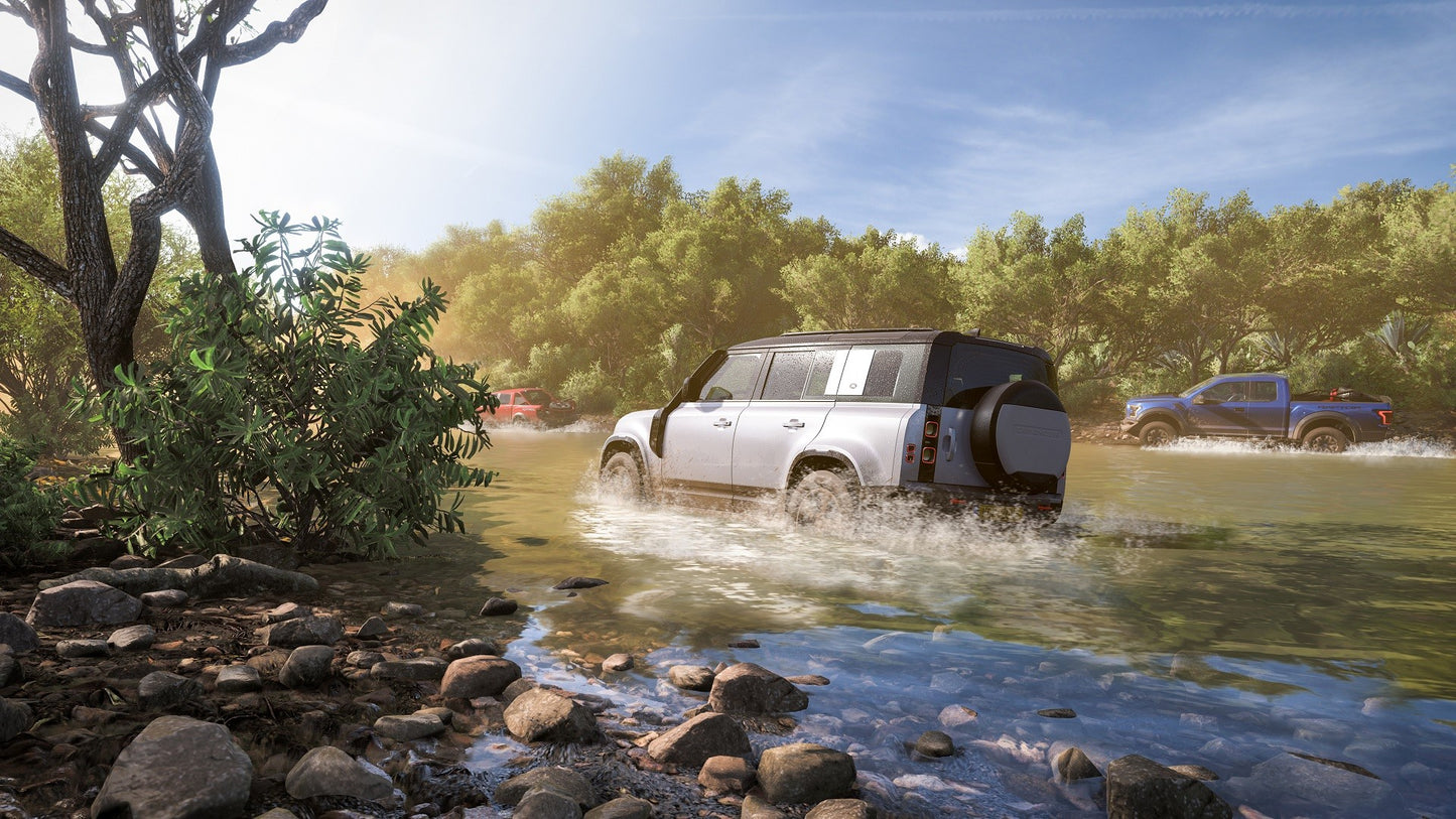 SUV driving through a shallow river with trees and clear sky in the background