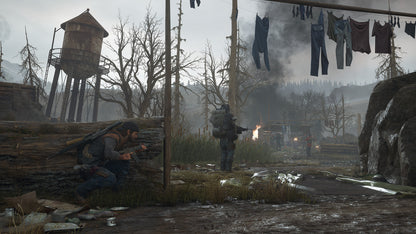 Two characters in a post-apocalyptic setting with a wooden structure, clothes hanging, and a fire in the background.