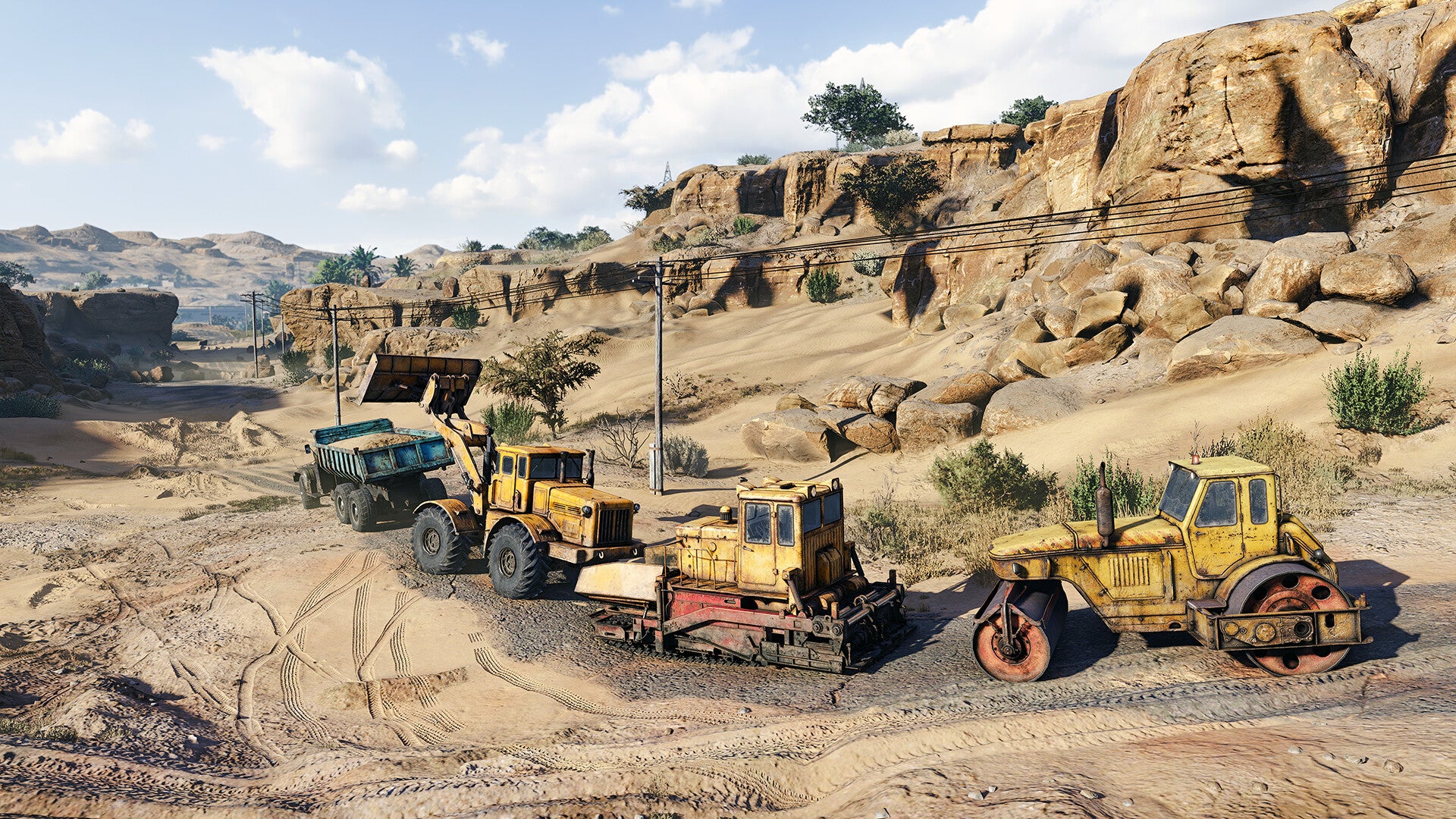Construction vehicles on a dirt road with rocky landscape and blue sky.